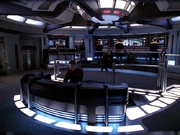 Die Brücke der USS Voyager - im Vordergrund die Steuerkonsole, im Hintergrund die taktische Station (links), Turbolift (Mitte) und die Plätze des Kommandanten und des Stellvertreters (rechts)